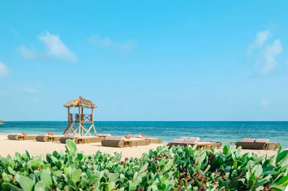 Beach scene with tiki-style lifeguard tower and woven lounge chairs on sand by turquoise water