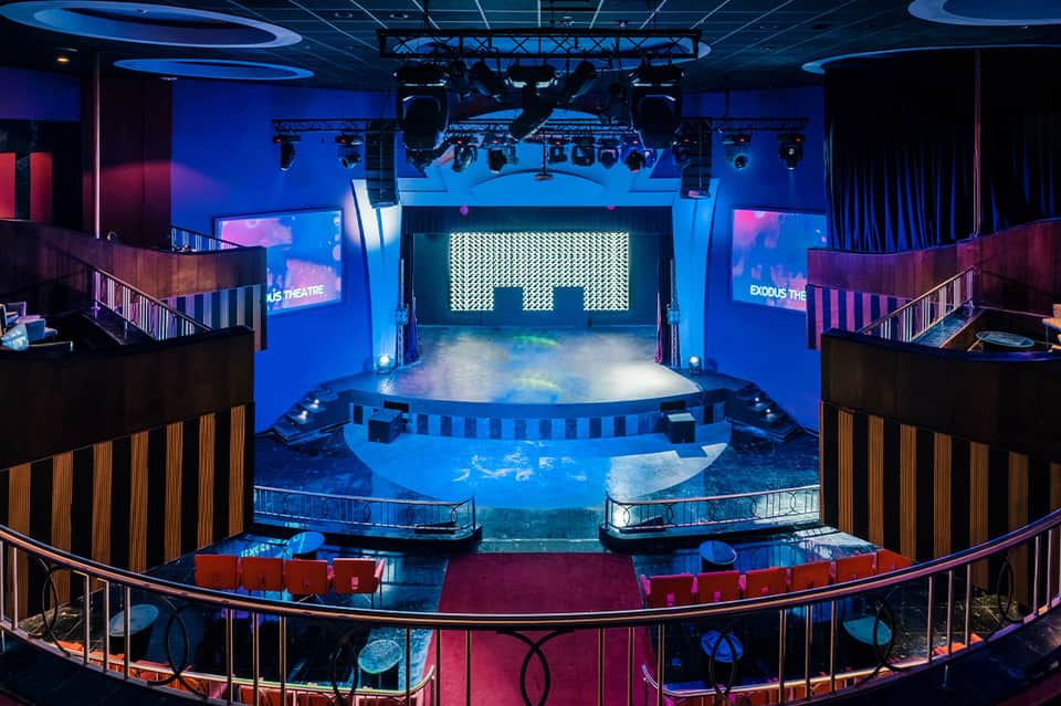 Modern theater interior with blue lighting, stage, and two-level seating areas