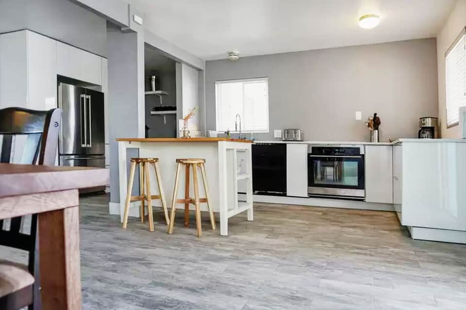 Modern kitchen with white cabinetry, stainless steel appliances, wooden bar stools, and gray wood flooring