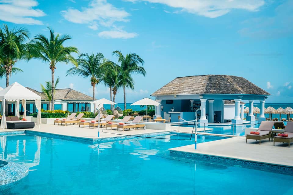 Luxury beachfront resort pool with turquoise water, white cabanas, palm trees, and ocean view