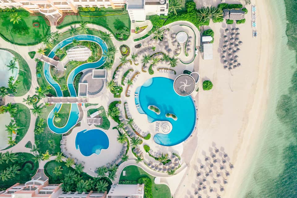 Aerial view of resort with multiple turquoise pools, landscaped grounds, and beachfront access
