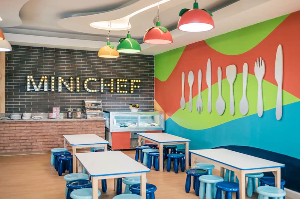 Colorful kids dining space with 'Mini Chef' sign, playful wall art, and colorful hanging lamps