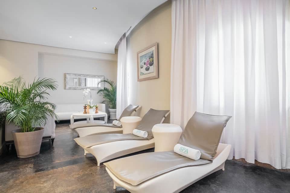 Spa relaxation room with cream-colored lounge chairs, plants, and sheer curtains