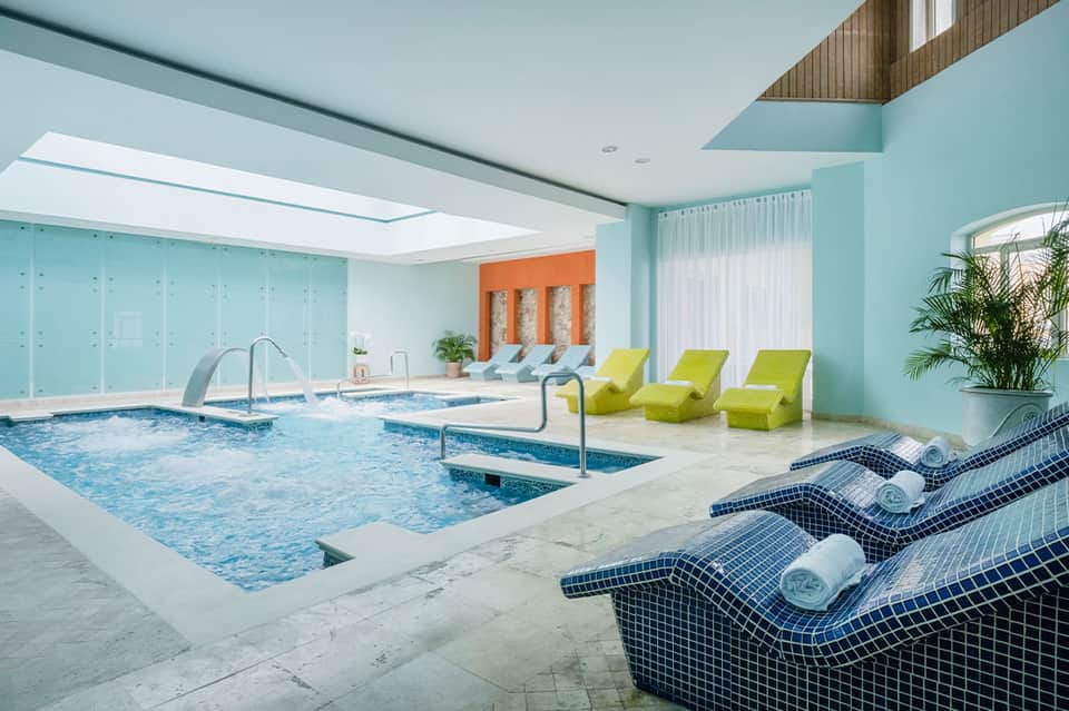 Indoor aquatic center with turquoise walls, lap pools, spa loungers, and natural skylight