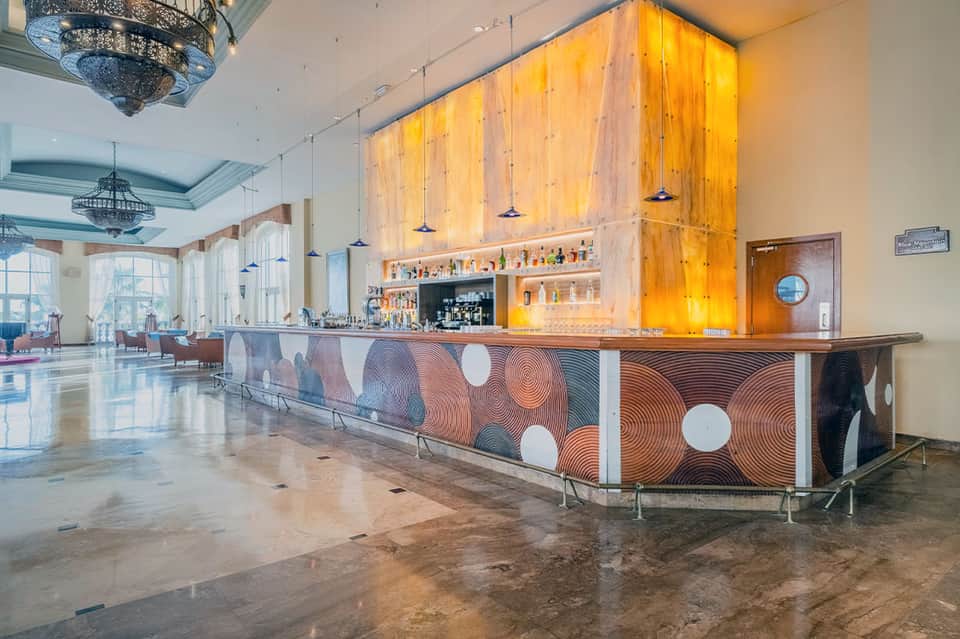 Modern hotel lobby featuring illuminated wooden wall, patterned bar front, elegant chandelier, and spacious interior