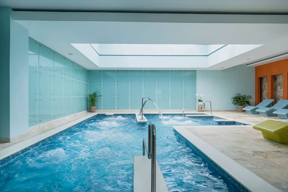 Modern indoor swimming pool with glass walls and spa area in contemporary resort facility