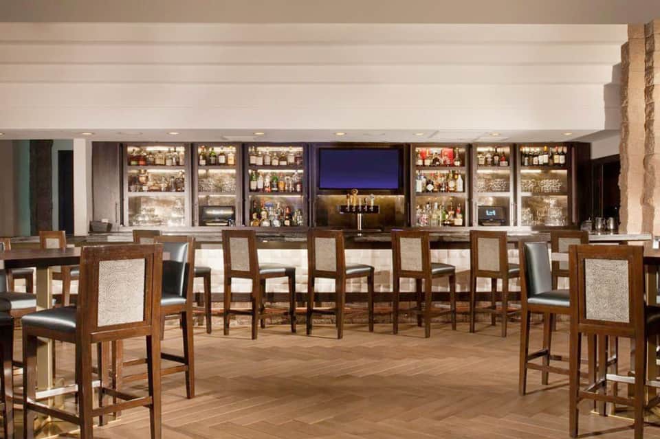 Hotel bar with wooden chairs and illuminated liquor shelving behind counter