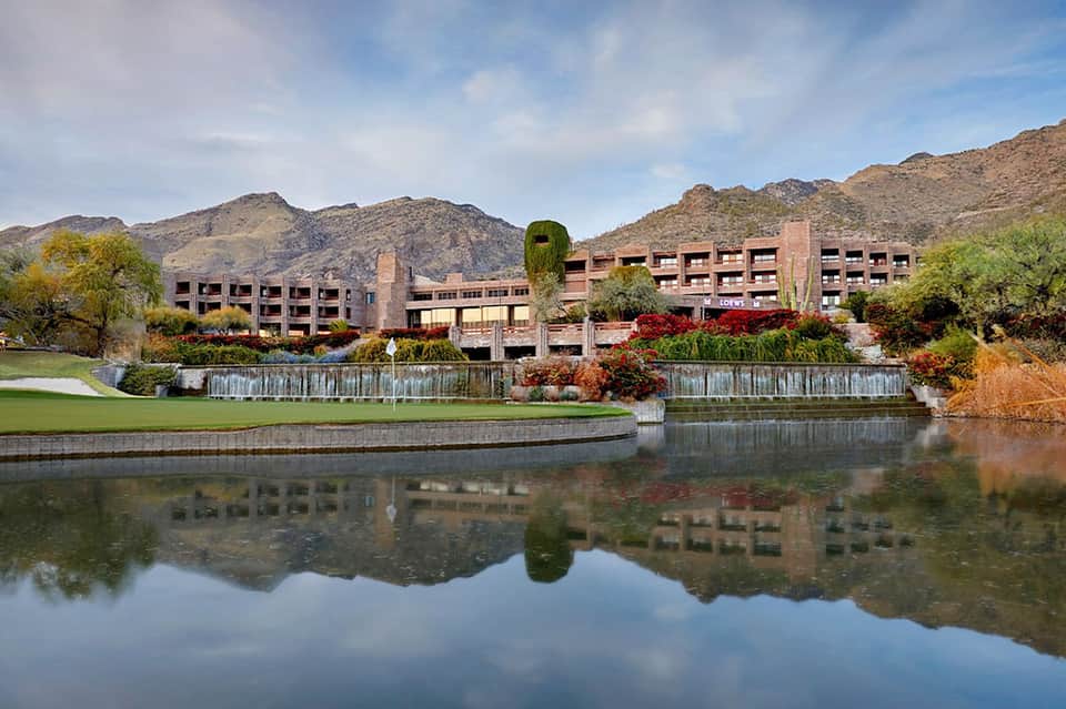 Desert resort exterior reflected in still water with mountains, landscaping, and modern building