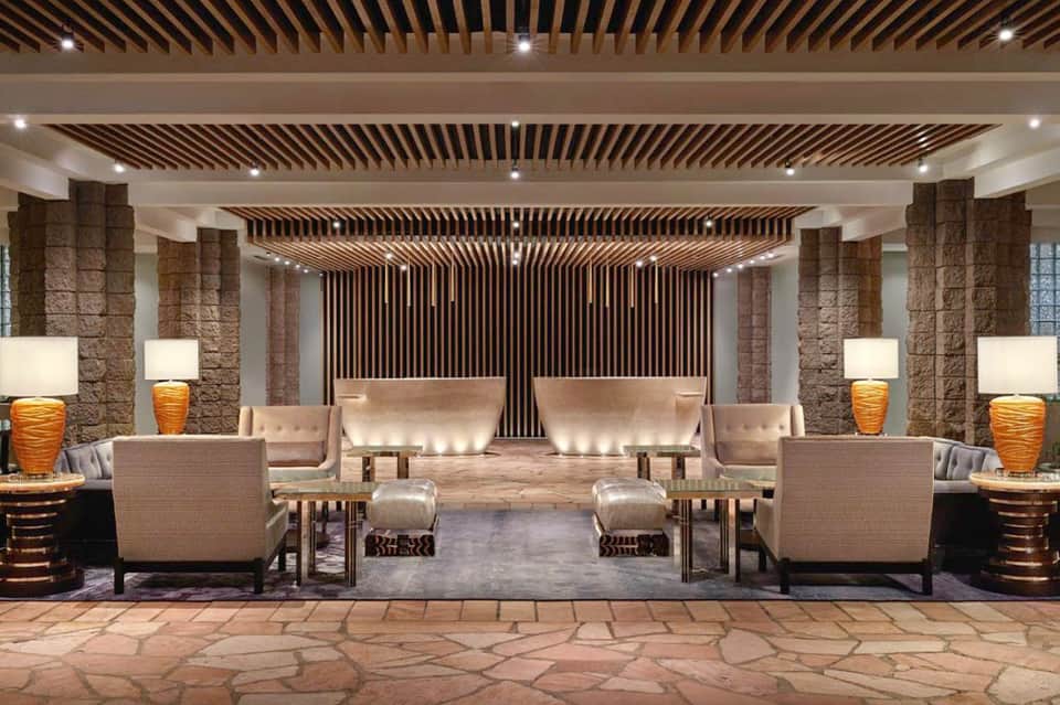 Luxurious hotel lobby featuring stone columns, wooden ceiling, beige seating, and ambient lighting.