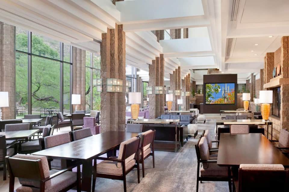 Modern lounge area with large windows, wooden columns, comfortable seating, and warm lighting