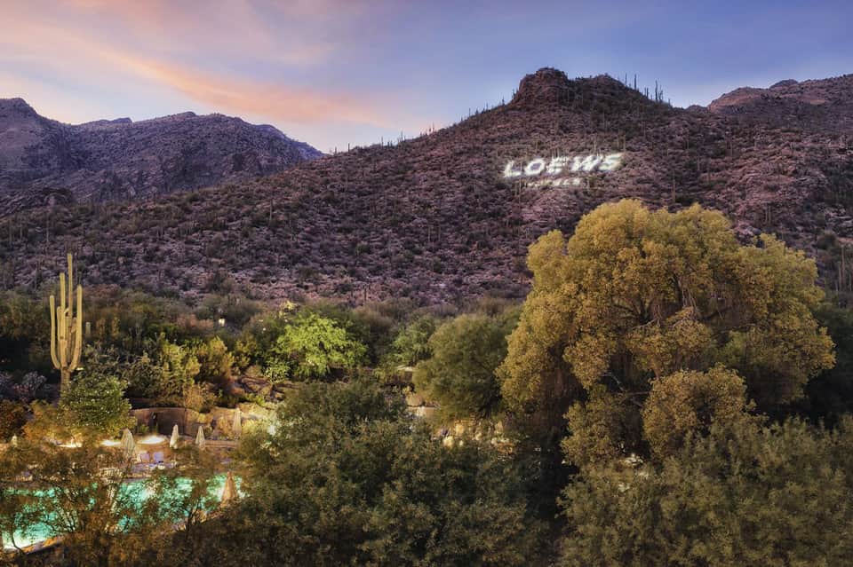Desert landscape at dusk with saguaro cacti, mountains, and a resort sign