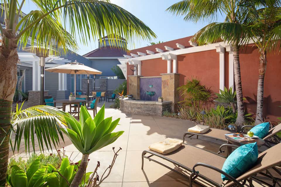 Tropical outdoor patio with lounge chairs, palm trees, coral wall, pergola, and water feature