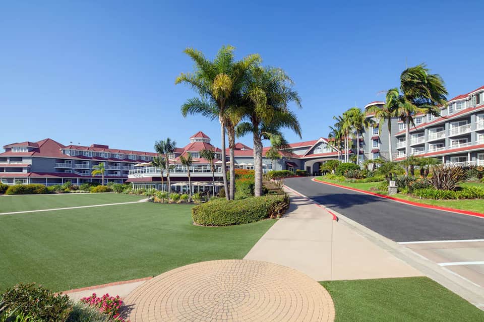 Resort entrance with golf course, palm trees, red-roofed main building, and tropical landscaping