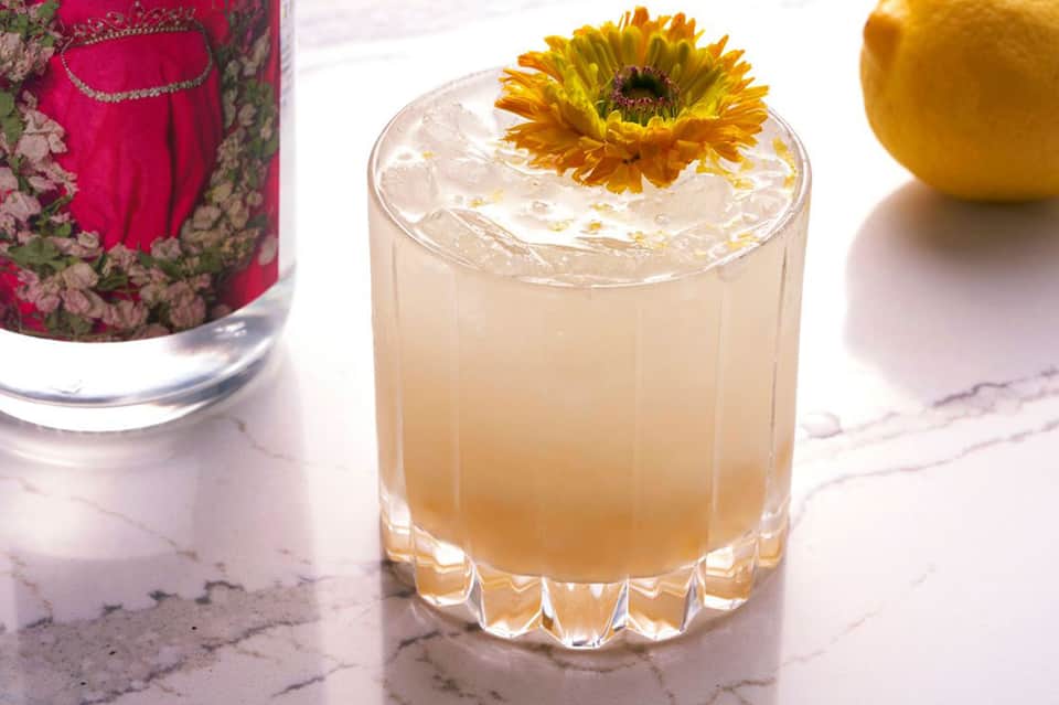 Refreshing cocktail with yellow flower garnish and citrus fruit on marble surface