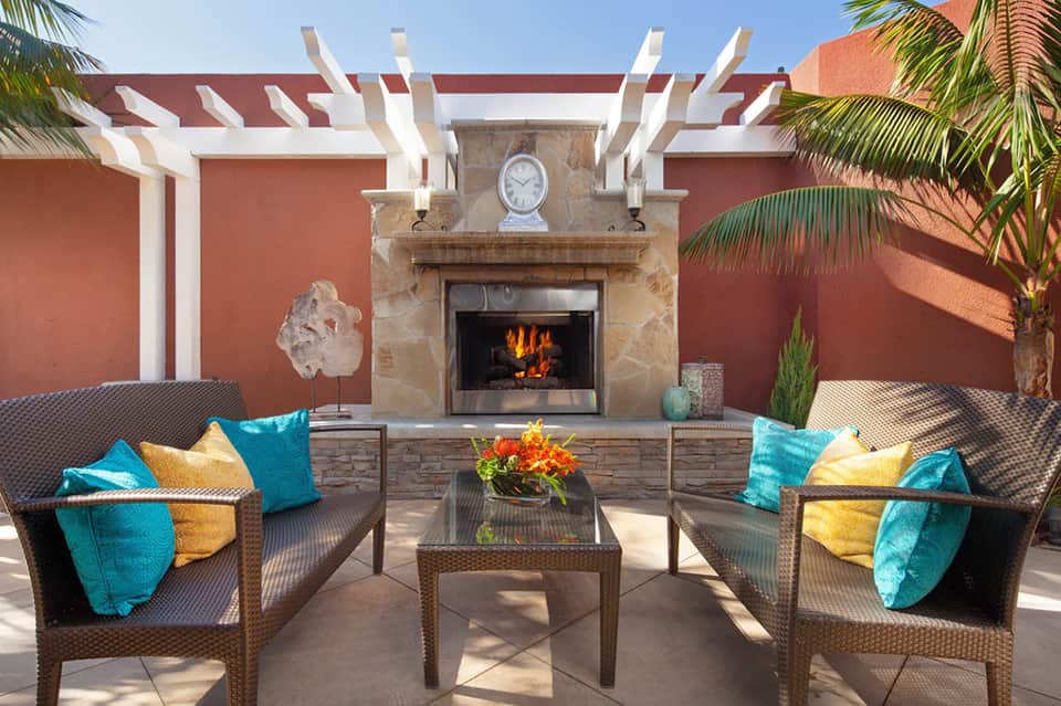 Outdoor patio lounge with fireplace, wicker seating, turquoise and yellow pillows, and terra cotta wall