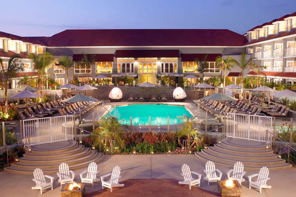 Resort pool at twilight with turquoise water, loungers, fire pits, and illuminated main building