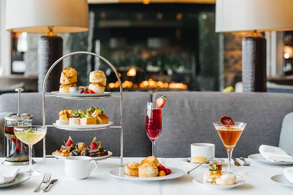 Elegant afternoon tea service with tiered pastries, cocktails, and fireplace ambiance