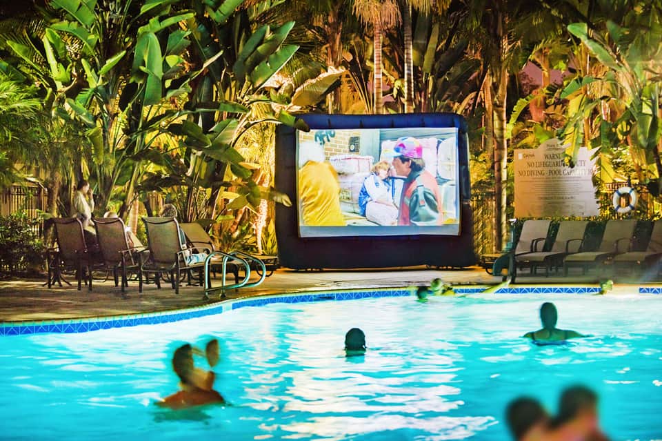 Indoor pool with tropical plants and large outdoor movie screen, guests swimming and relaxing