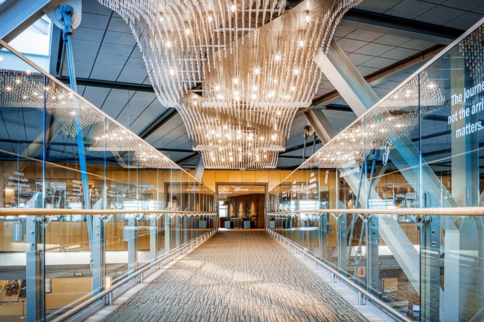 Contemporary corridor with dramatic woven chandelier, glass railings, skylights, and minimalist design aesthetic