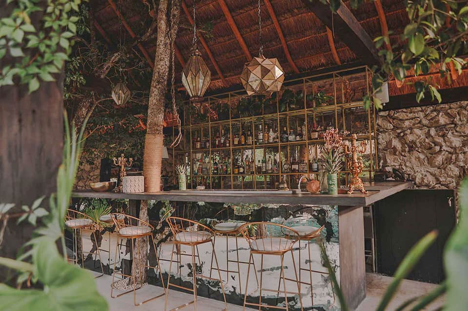Tropical bar with thatched roof, geometric lanterns, and palm tree surrounded by greenery