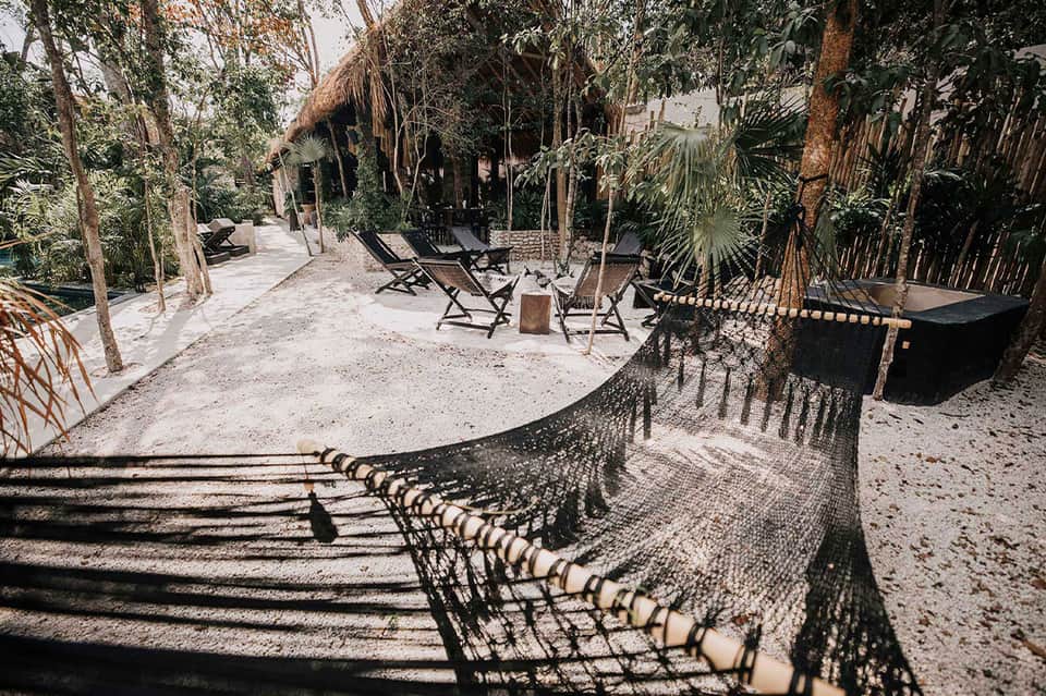 Sandy beach lounge area with hammocks, tiki huts, and tropical vegetation