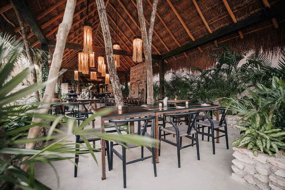 Rustic indoor dining area with thatched roof, wooden beams, and woven pendant lights