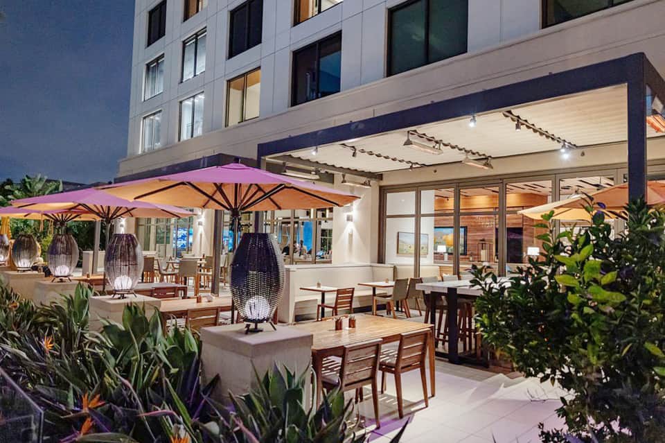 Upscale outdoor dining patio with purple umbrellas, string lights, and modern architecture