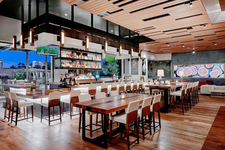 Contemporary bar and dining area with wooden tables, red chairs, and full liquor shelves