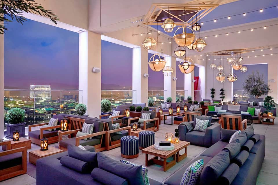 Upscale lounge with city skyline views, hanging pendant lights, and purple seating