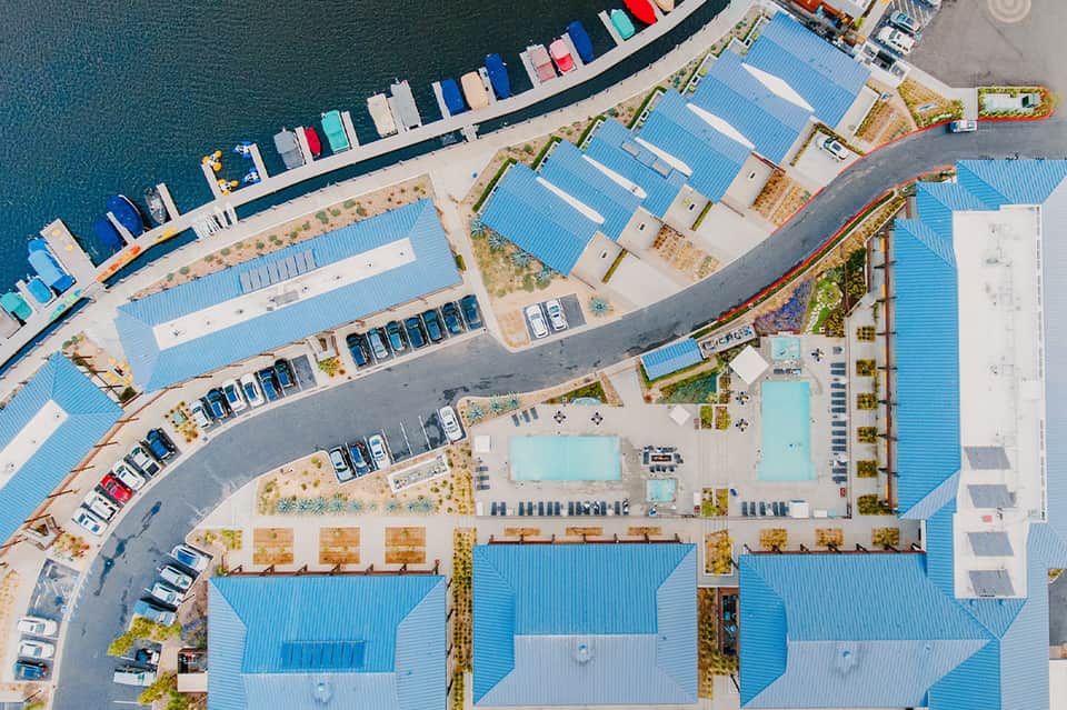 Aerial view of waterfront resort with pools, parking, blue roofs, and moored boats