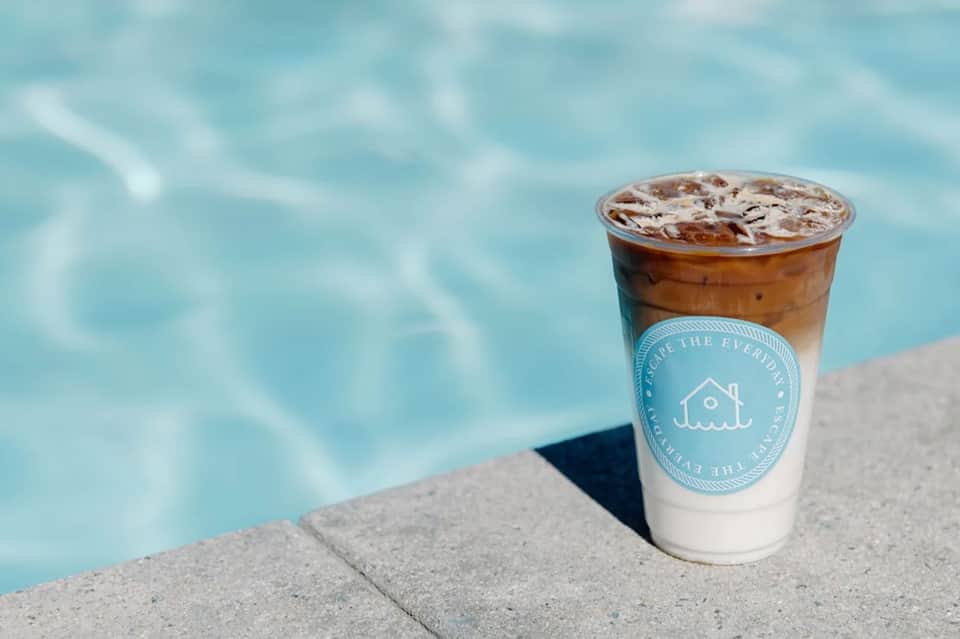 Iced coffee drink on pool deck edge with turquoise water rippling in background
