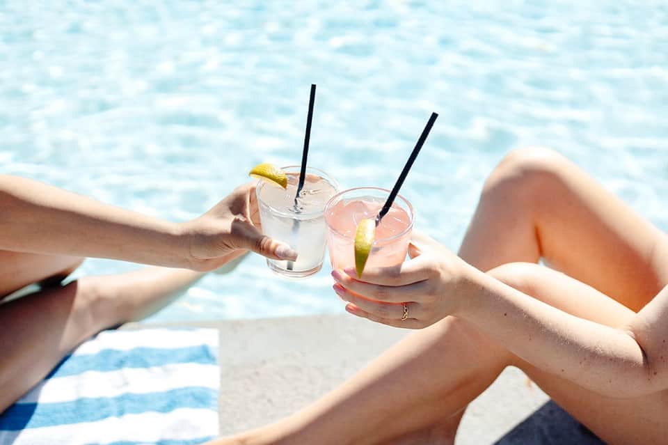 Two hands holding tropical cocktails with lime garnish over ocean background at beach