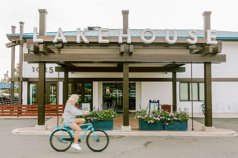 Lake House storefront with wooden pergola, white building, blue roof, and person on bicycle