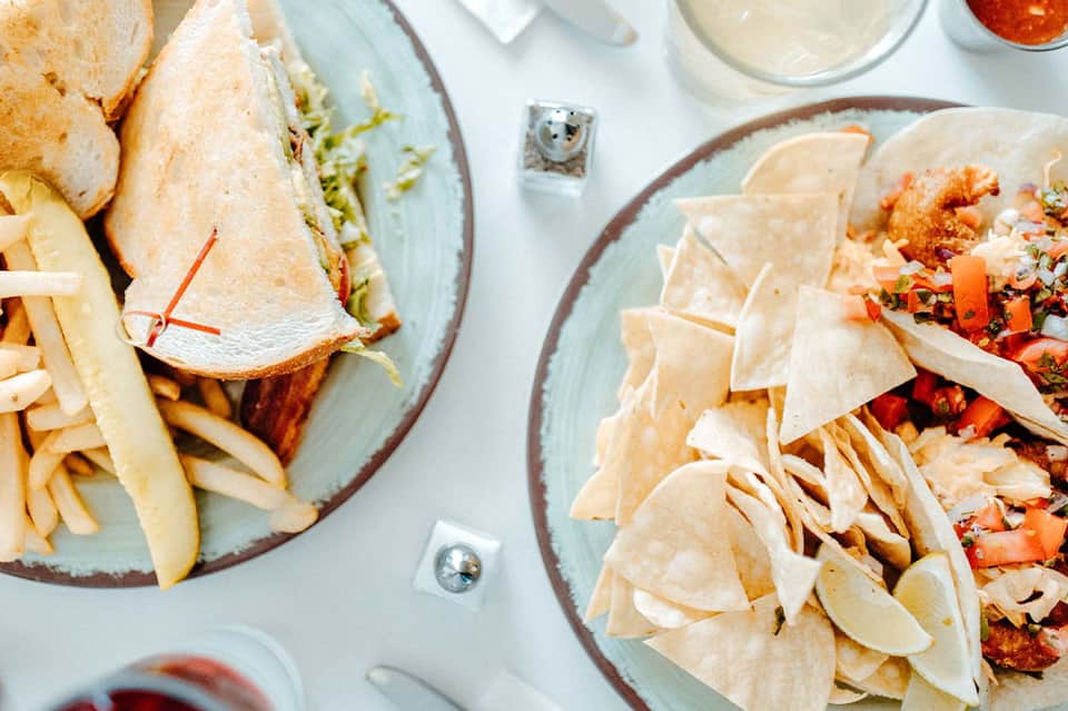 Overhead view of plates with tacos, fries, and Mexican dishes on white table