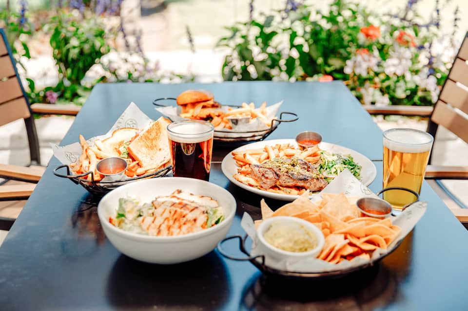 Outdoor dining table with seafood dishes, beer, and tropical drinks overlooking resort gardens