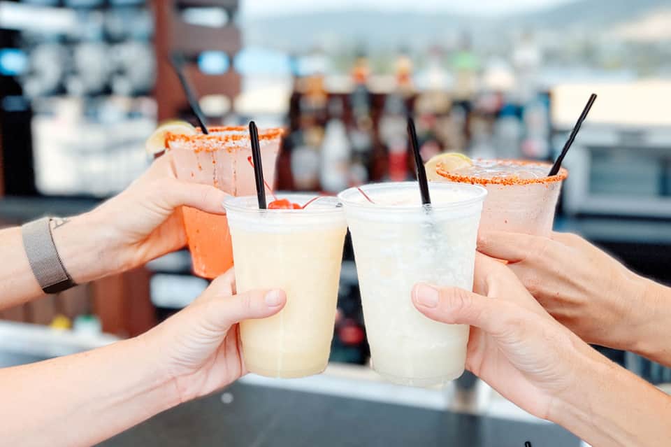 Hands toasting colorful frozen cocktails with salt-rimmed glasses at beach bar