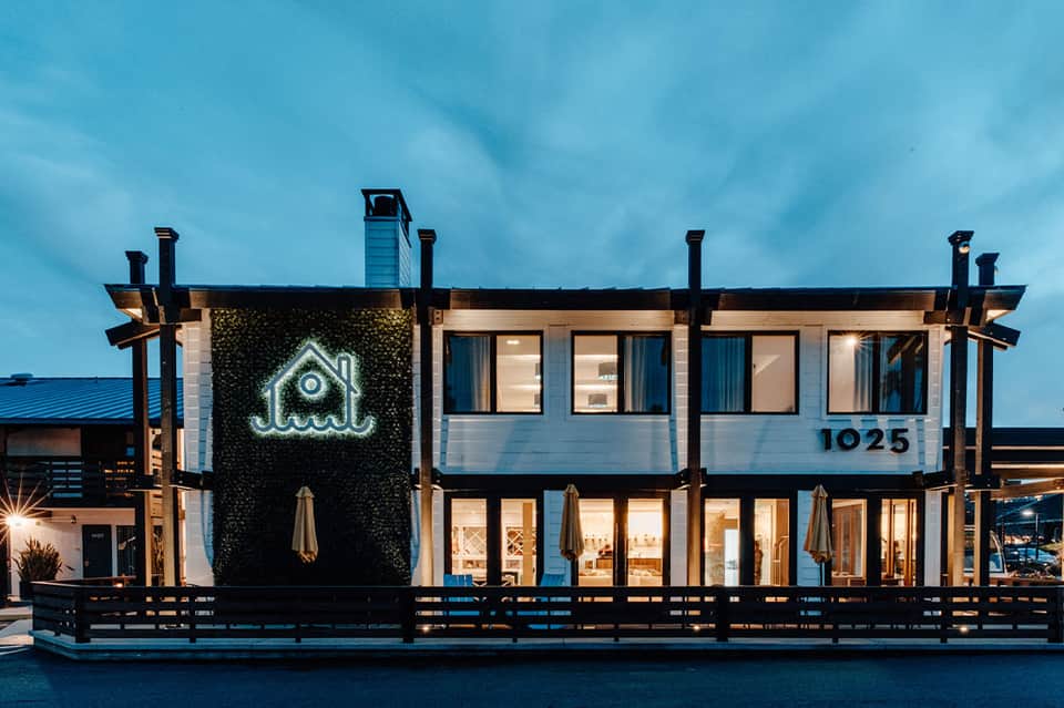 Modern waterfront restaurant with neon house sign, glass windows, and blue evening lighting