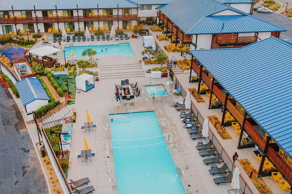 Aerial view of resort pools, cabanas, buildings with blue metal roofing, and manicured landscaping