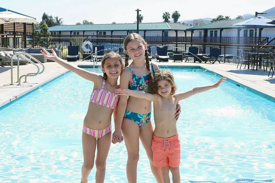 Three children in swimwear posing happily in resort pool area