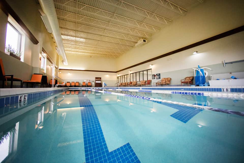 Bright indoor lap pool facility with lane dividers, seating, and natural skylight