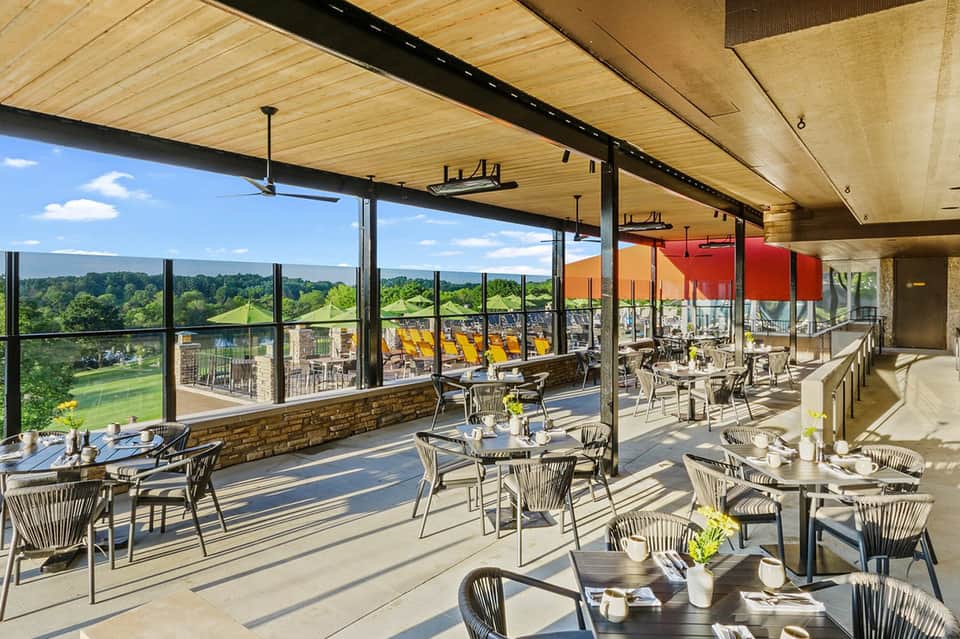 Modern restaurant terrace with floor-to-ceiling windows, yellow umbrellas, green landscape views