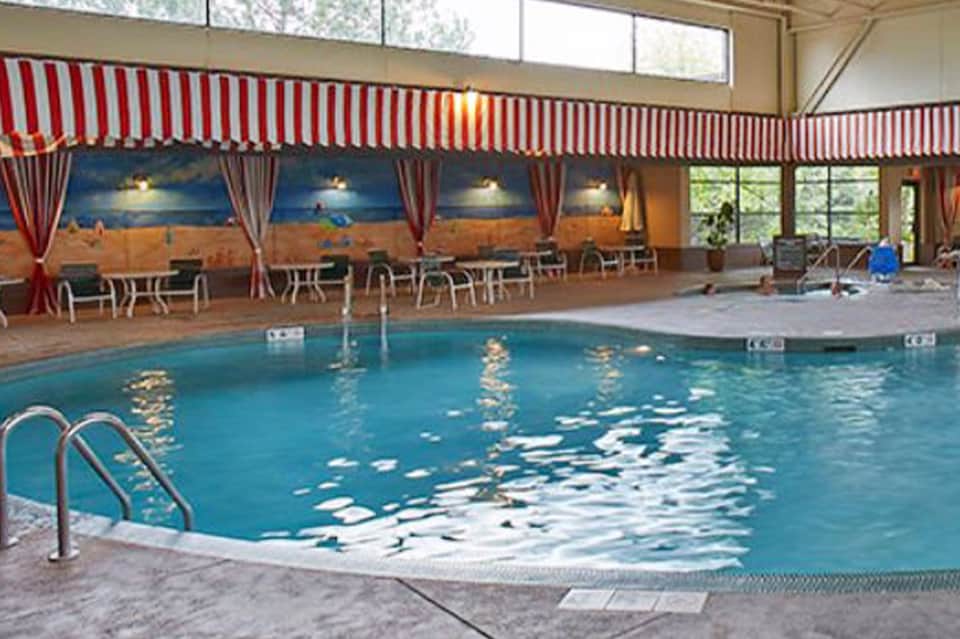 Indoor swimming pool with red and white striped awning, beach mural, lounge chairs, and natural light from windows