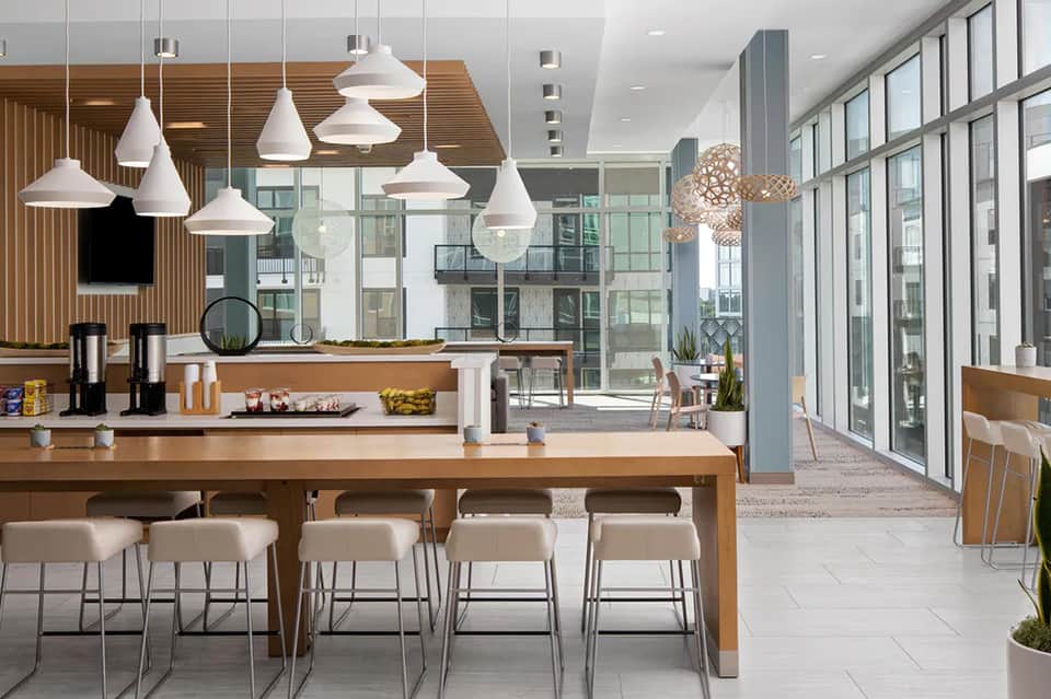 Contemporary hotel lobby café with wooden accents, white pendant lights, and floor-to-ceiling windows