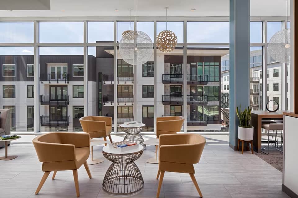 Modern lounge area with tan seating, hanging pendant lights, and floor-to-ceiling windows