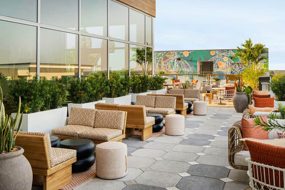 Contemporary outdoor lounge area with wooden furniture, colorful wall mural, and palm plants