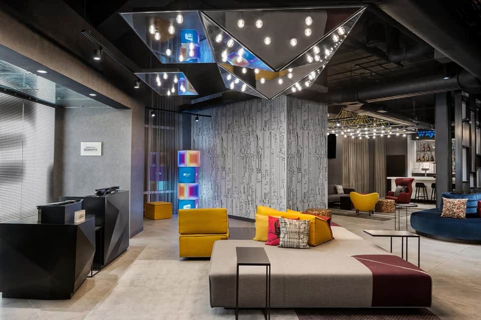 Modern hotel lobby with colorful seating, geometric ceiling lights, and contemporary design