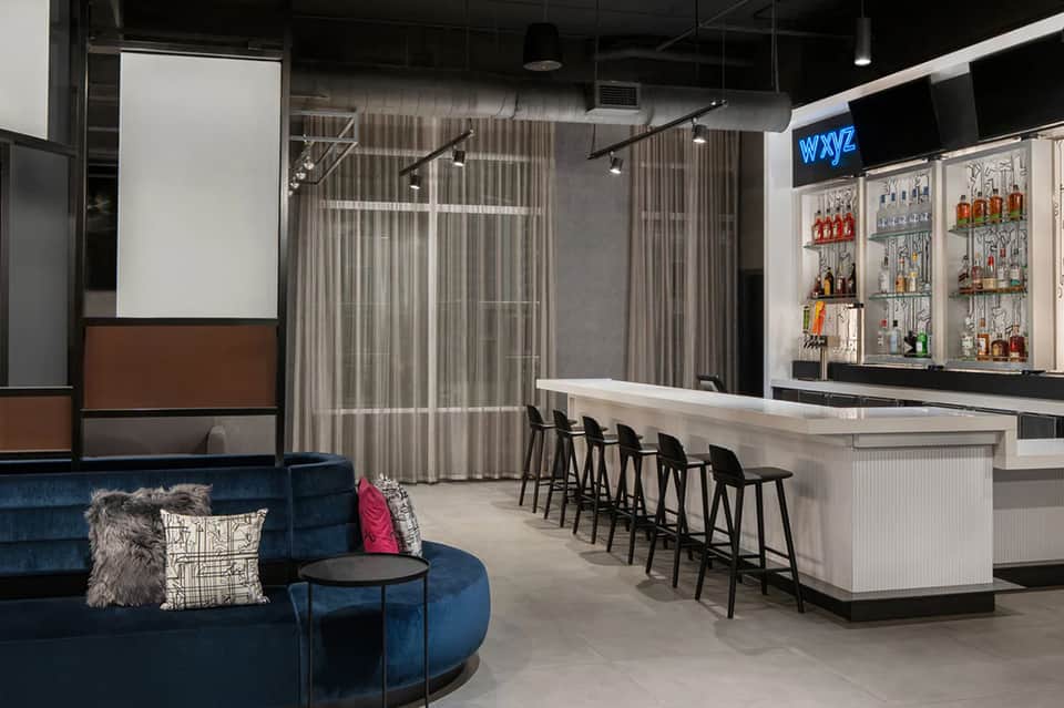 Contemporary hotel bar with blue velvet seating, full liquor shelves, and lounge area