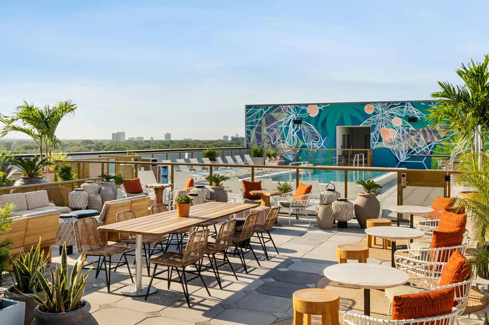 Rooftop terrace with colorful seating, wooden tables, city skyline views, and mural accent wall