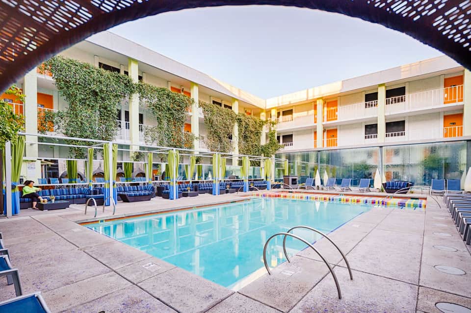 Indoor hotel pool with turquoise water, surrounding loungers, ivy-covered walls, and modern courtyard architecture