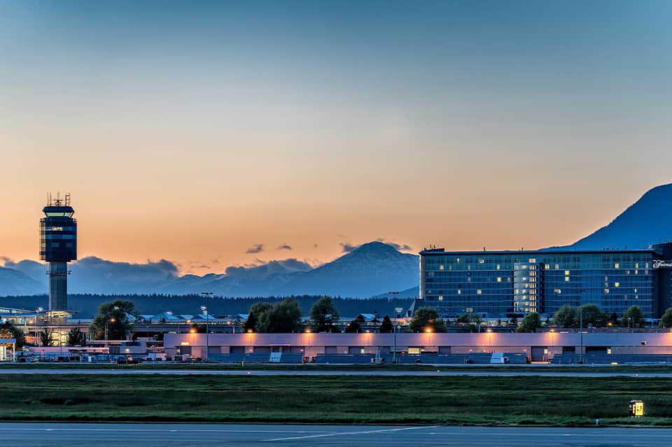 Hotel exterior at dusk with illuminated building, mountains, and control tower backdrop